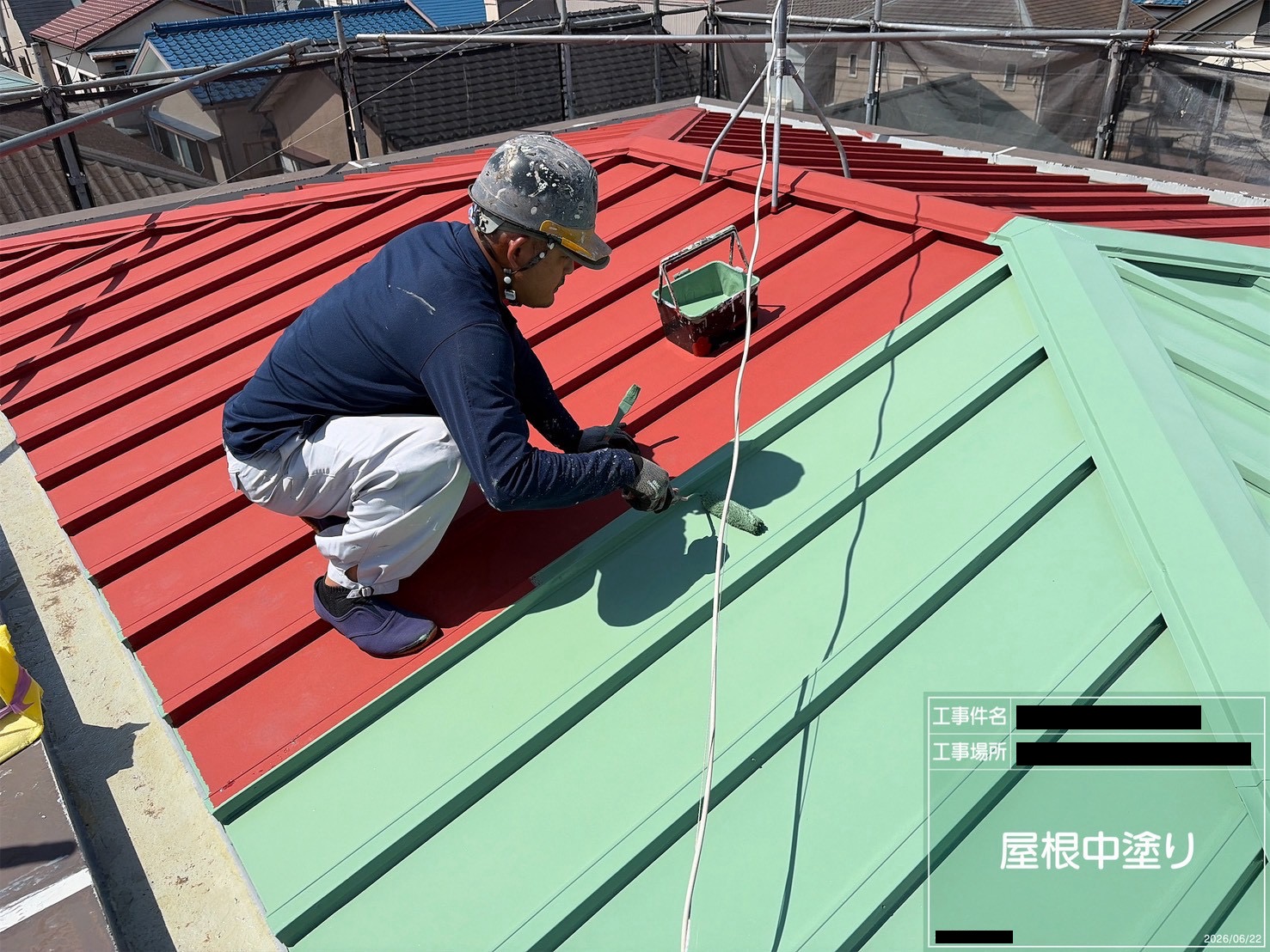 赤い錆止めの上に緑色の中塗りを塗り重ねる屋根塗装の様子
